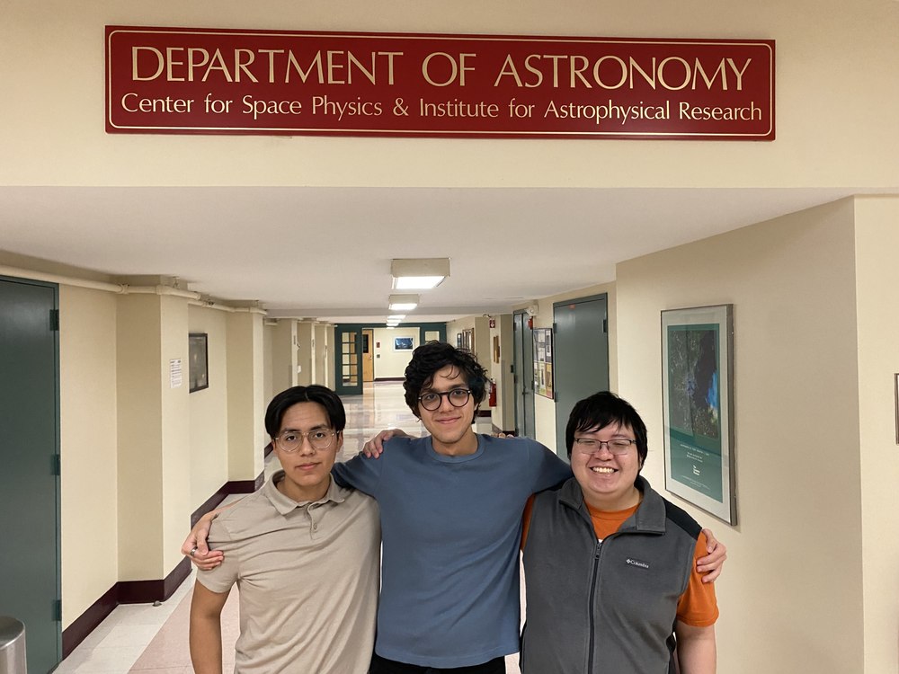Three group members posing under the Department of Astronomy sign in the hallway.